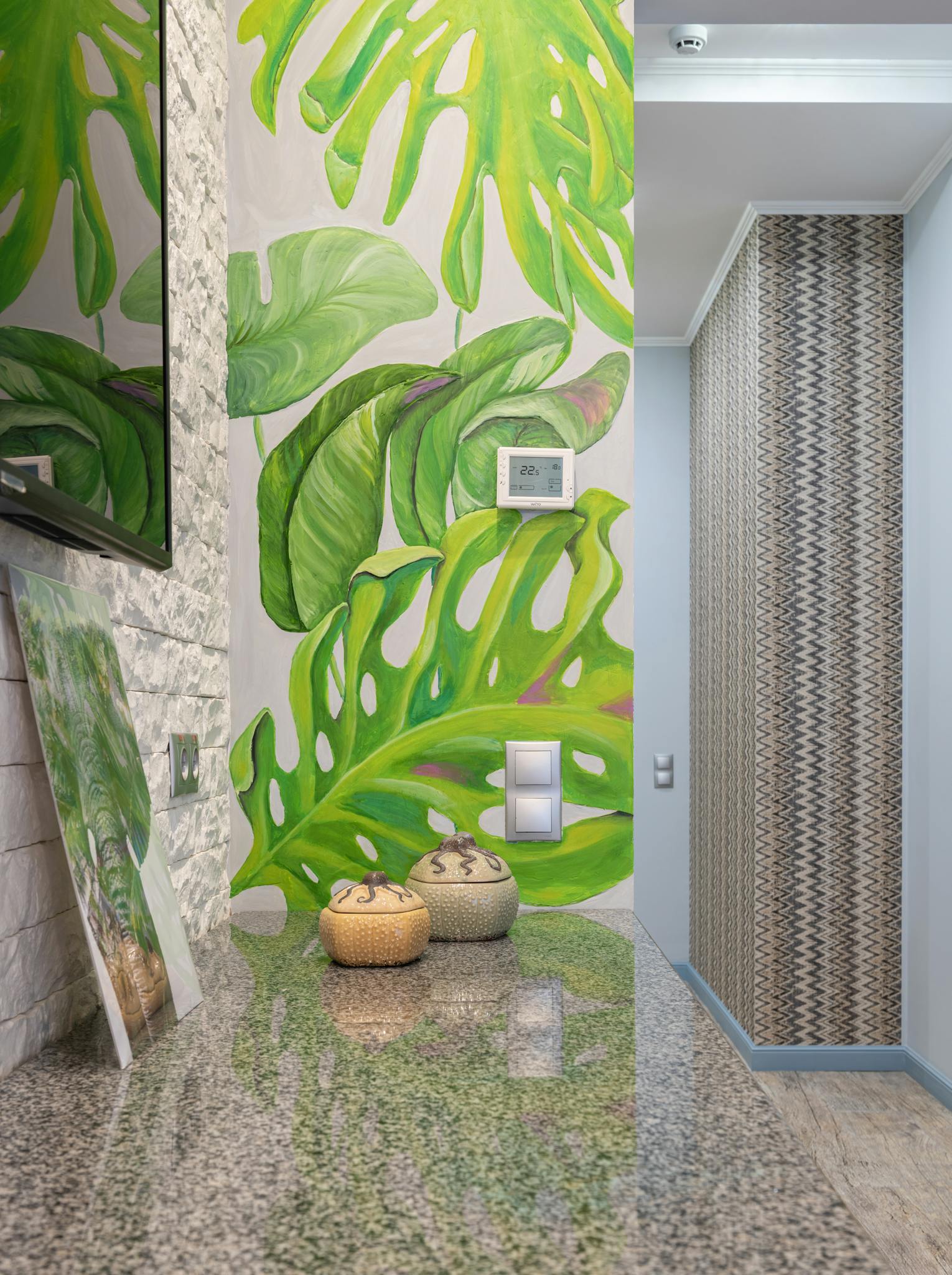 Vibrant tropical leaf mural on a wall in a stylish interior space with decorative accents.